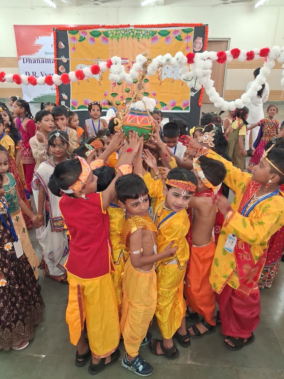 Students in yellow and red costumes lifting a decorated pot during a festival